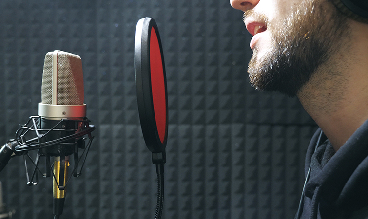 Male singer in headphones singing song into a microphone at a sound studio