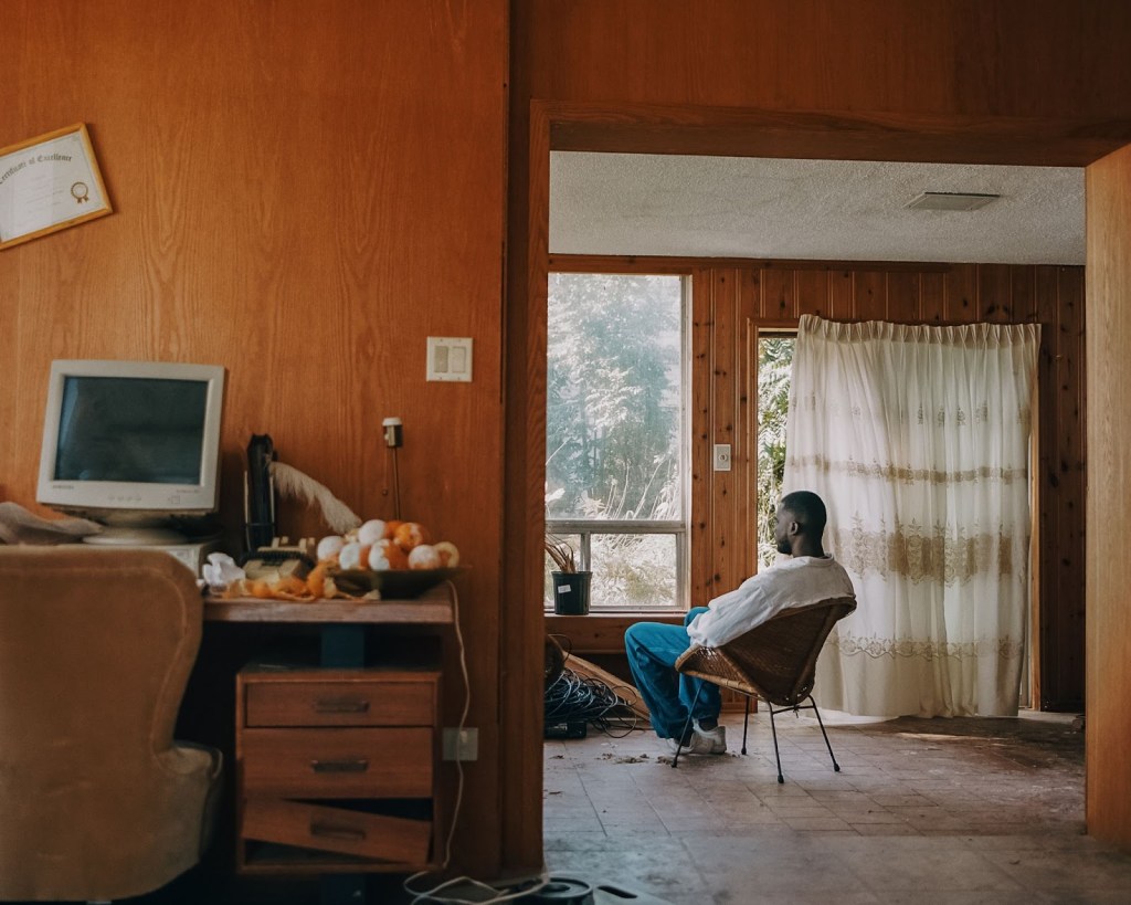 A man sits in a dusty old house looking out the window despondently
