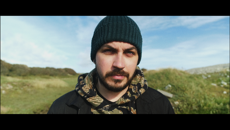 Man looks concerned at the camera with a landscape scene in the background