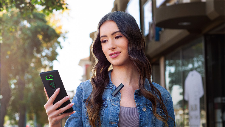 Pretty woman standing outdoors wearing a lav mic videoing herself on cellphone