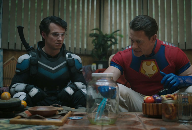 Two super heroes sitting at a table together in the series Peacemaker