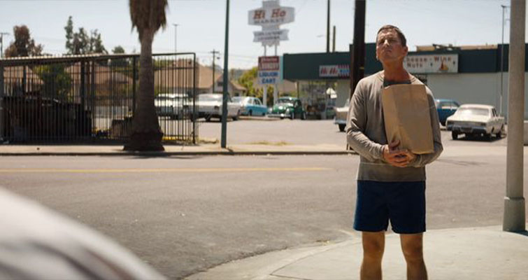 A scene from Ford vs. Ferrari of Ken standing in the street with bright afternoon sun.