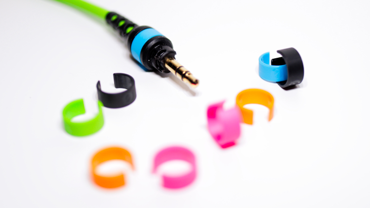 Blue, black, orange, green, and pink cable rings with a green cable on a white backdrop